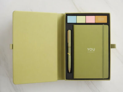 Premium corporate stationery gift set in olive gold magnetic closure box revealing branded notebook pen and highlighters on white marble