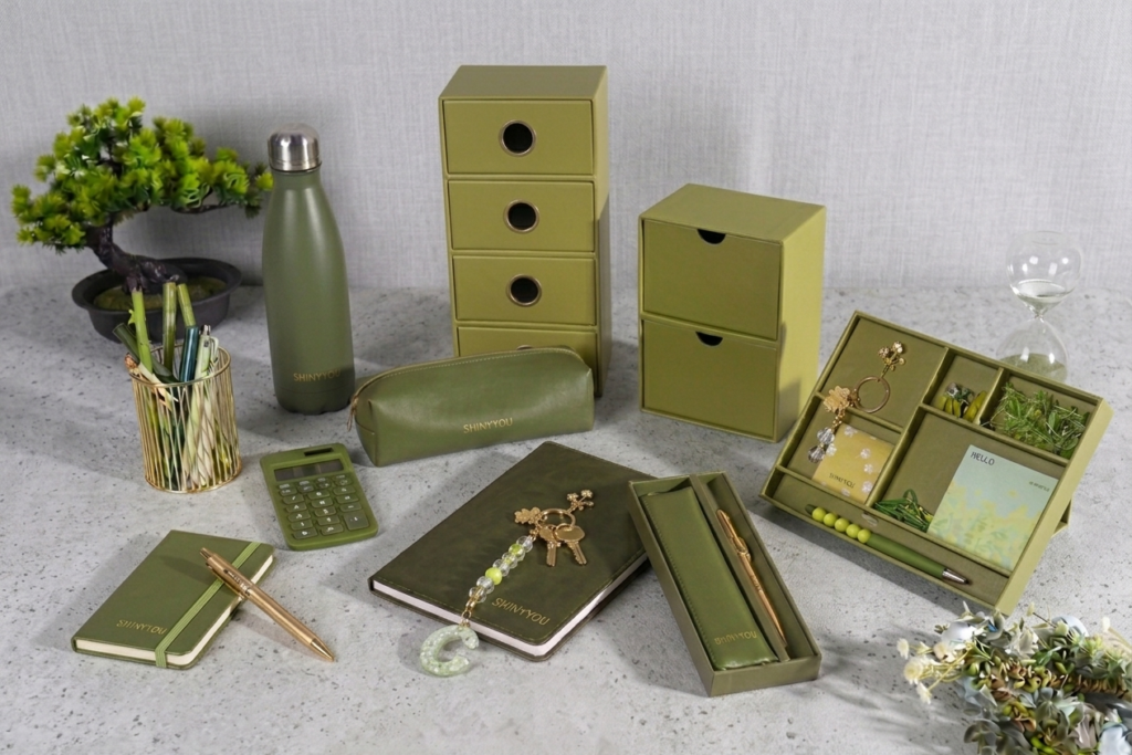 Minimalist wholesale stationery set featuring olive green office organizers, notebooks, a water bottle, and desktop accessories arranged as a flat-lay on a clean studio surface.