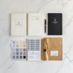 Wholesale Stationery Manufacturer 87 Private label manufacturer stationery process showing branded notebooks journals and packaging samples on white marble desk with specification sheets and Pantone color swatches